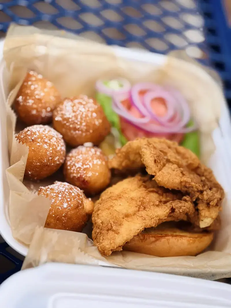 Fried fish sandwich with lettuce, tomato and onion, served with hush puppies